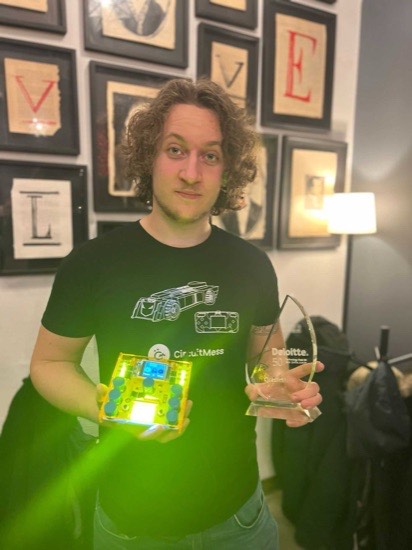 Albert Gajšak holding a glass Deloitte trophy in one hand and a glowing green CircuitMess kit in the other.