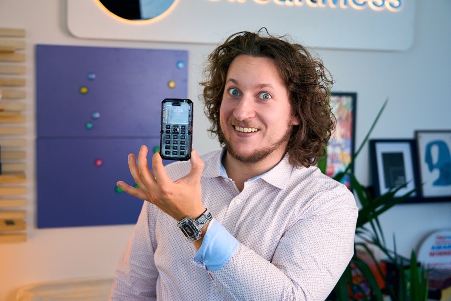 Albert Gajšak grinning widely while holding up a clear-cased MAKERphone.