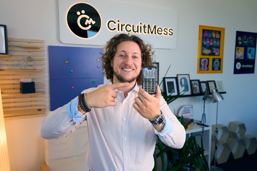 Albert Gajšak pointing at a MAKERphone he is holding, under the CircuitMess logo.
